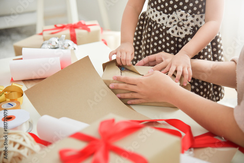 Young mother and her daughter hands wrapping a gift box.