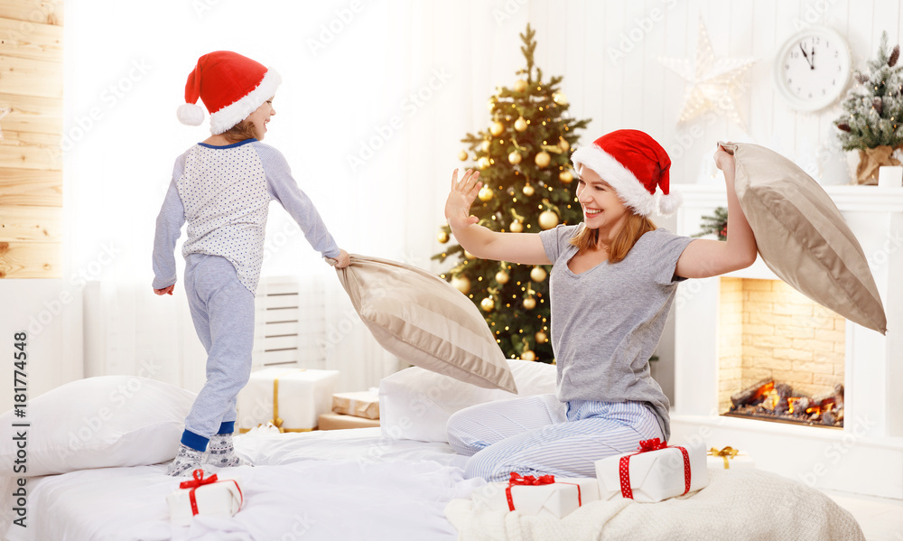 Fototapeta premium happy family mother and child daughter at christmas morning fighting pillows in bed