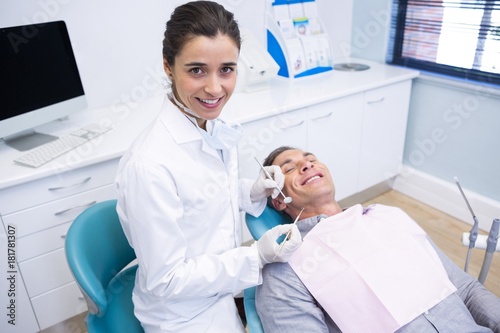 Portrait of dentist holding equipment while standing by patient