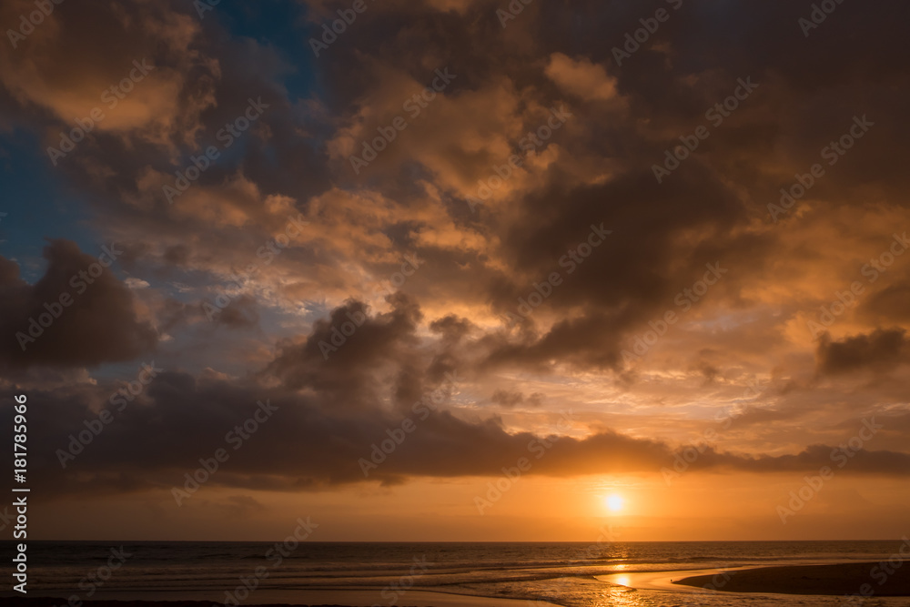 Dramatic sunset clouds reflected on the water sea. Tropical beach landscape at golden hour