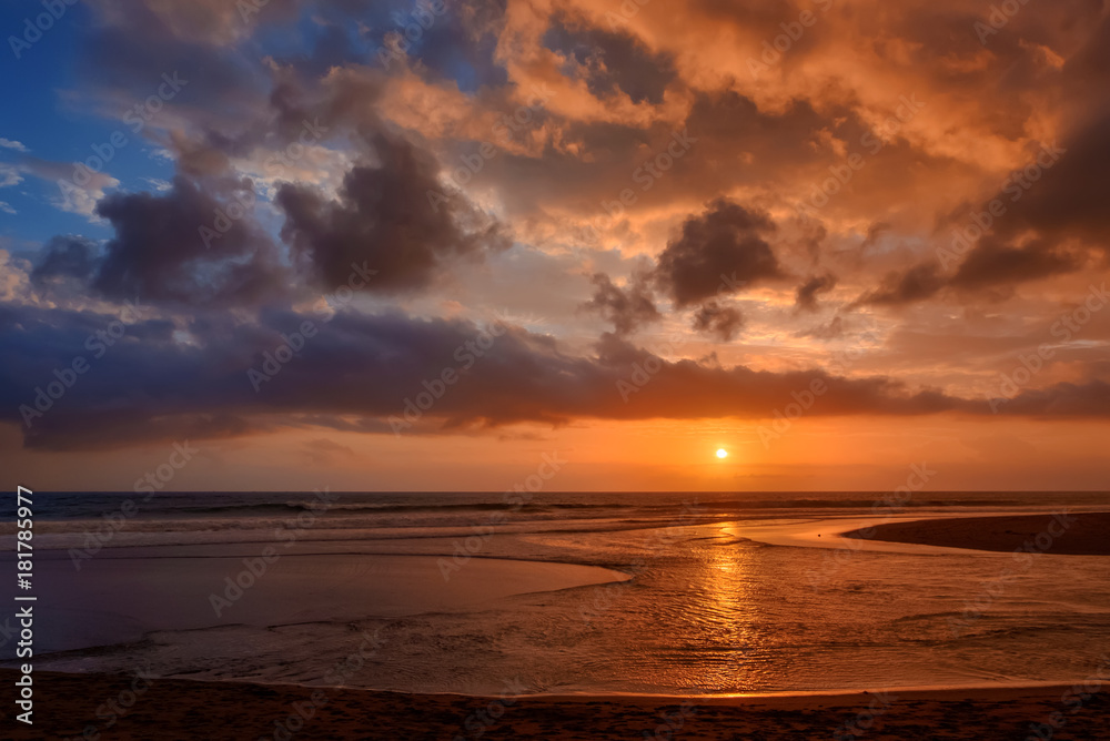 Fototapeta premium Dramatic sunset clouds reflected on the water sea. Tropical beach landscape at golden hour