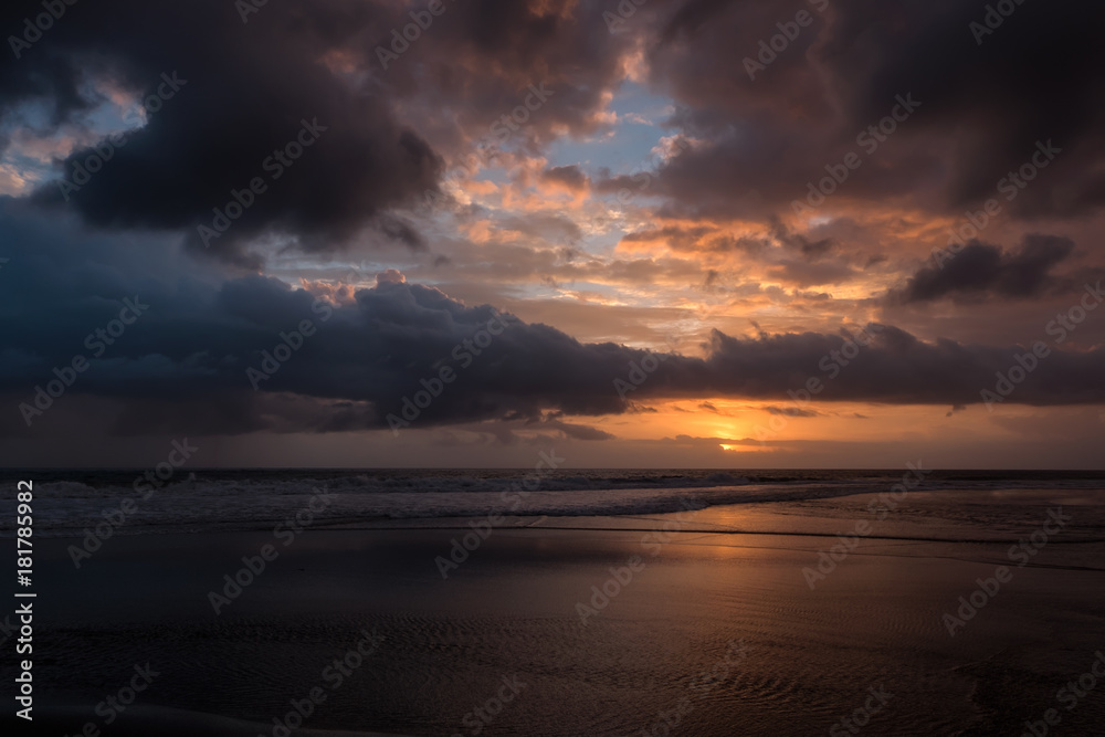 Dramatic sunset clouds reflected on the water sea. Tropical beach landscape at golden hour