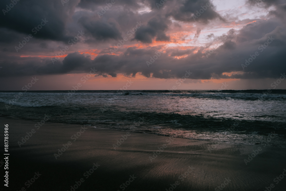 Dramatic golden sunset clouds reflected on the water sea. Tropical beach landscape at dusk