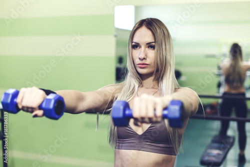 Young blonde woman doing exercises with dumbbells in a GYM.