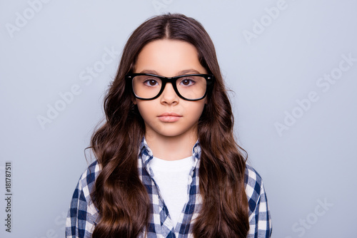 Close up portrait of beautiful, serious, little girl looking at camera, having health problem with her eyes, standing over grey background