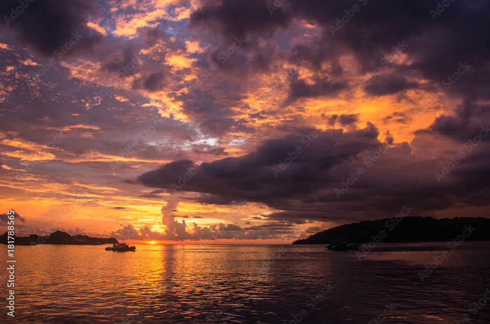 A fiery sun is setting in the bay of Kota Kinabalu, Borneo, colorizing the cloudy sky in a dramatic fashion