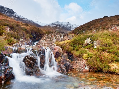 Rapids in small waterfall on stream, Higland in Scotland an early spring day. Snowy mountain peaks
