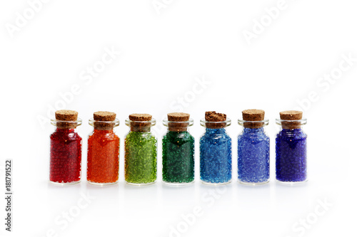 Seven tiny glass bottles with a cork stopper, filled with a rainbow colours of beads, on a white background photo