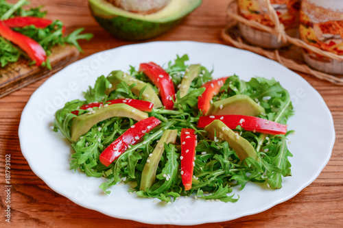 Avocado, arugula and red pepper salad on a white plate. Homemade arugula and avocado salad with red pepper and sesame seeds. Raw food diet. Veganism. Closeup