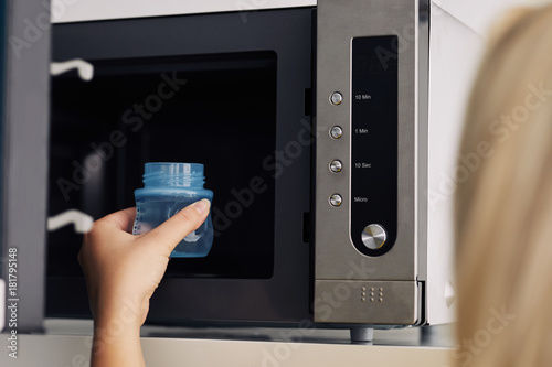 Mother putting a baby bottle with water into a microwave