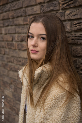 Young girl portrait with winter coat next to brick wall