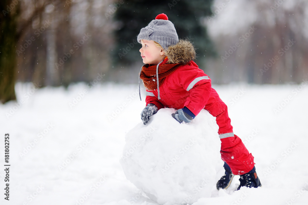 Little boy in red winter clothes having fun with snowman