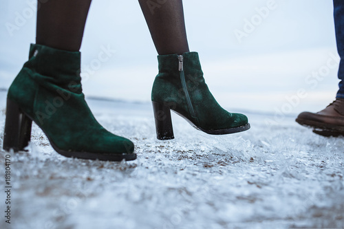 Winter is coming. Female and male boots on rough ice surface. Closeup. Two friends or lovers standing on beach covered fresh ice