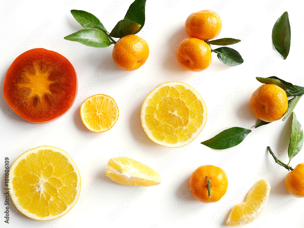 Creative flat layout of fruit, top view. Sliced orange, lemon, persimmon, tangerine, green leaves isolated on white background. Food wallpaper, composition pattern of fresh fruits. Creative flat layout of fruit, top view. Sliced orange, lemon, persimmon, tangerine, green leaves isolated on white background. Food wallpaper, composition pattern of fresh fruits.
