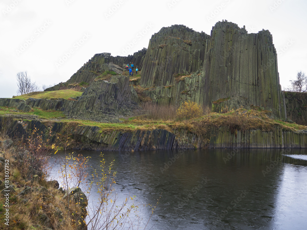 basalt pillars lava vulcanic rock formation organ shape with lake panska skala and group of tourist in blue jacket in kamenicky senov prachen czech republic