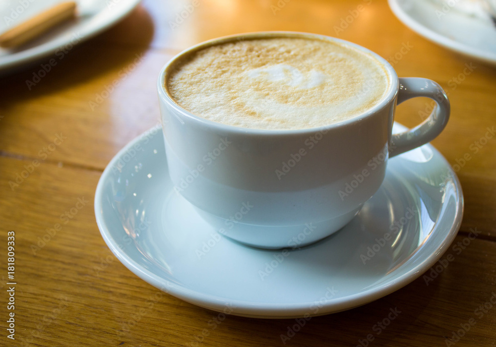 White cup of coffee on wooden table background, front view. Cappuccino latte in cafeteria. White cup of coffee on wooden table background, front view. Cappuccino latte in cafeteria.