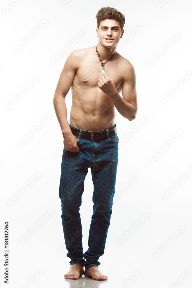 Male beauty & Blue jeans concept. Handsome smiling model in trendy jeans with perfect muscular body posing over white background. Leather accessories. Urban style. Full length portrait Male beauty & Blue jeans concept. Handsome smiling model in trendy jeans with perfect muscular body posing over white background. Leather accessories. Urban style. Full length portrait