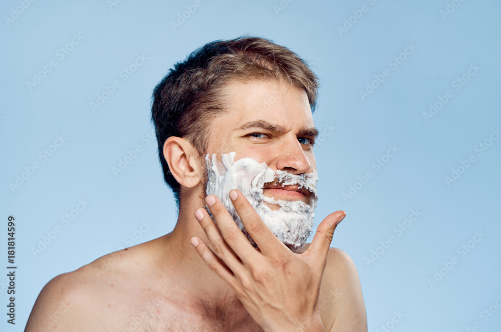 A young guy with a beard on a blue background applies shaving foam