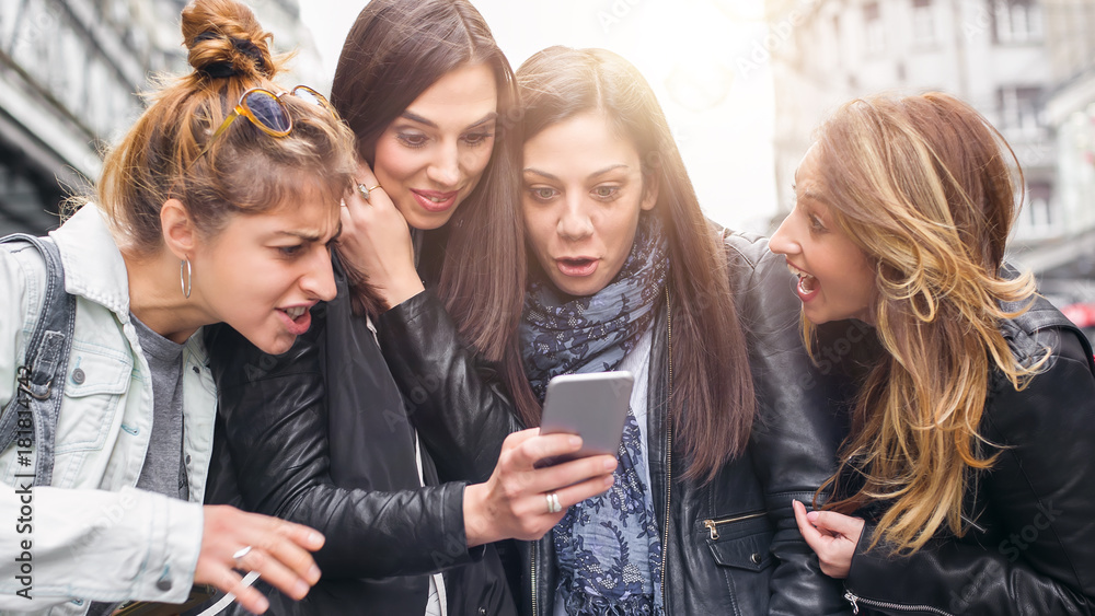 Happy four friends walking on the street and using cellphones