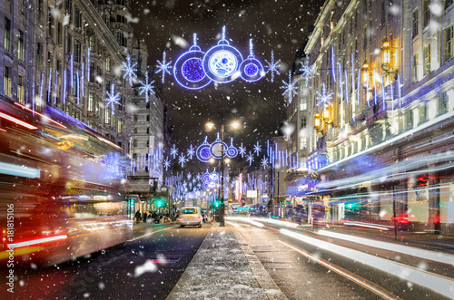 Festlich geschmückte Einkaufsstraße in London mit vorbeifahrendem Bus und Schneefall
