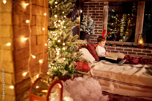 A child little boy is reading a book in the Christmas room.