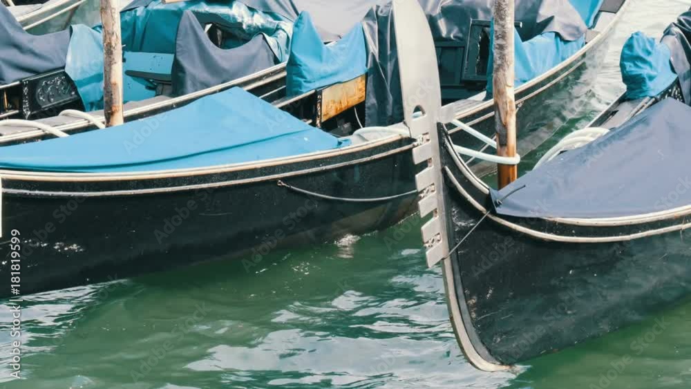 Venetian gondola covered in blue cloth while docking on the canal in Venice Italy, Noses moored gondolas neatly standing in a row Venetian gondola covered in blue cloth while docking on the canal in Venice Italy, Noses moored gondolas neatly standing in a row