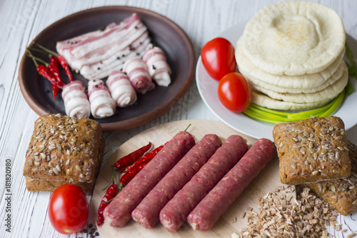 Smoked sausage, bacon and tomatoes on a wooden table photo
