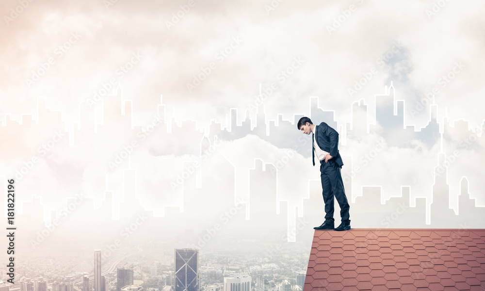 Businessman looking down from roof and modern cityscape at backg Businessman looking down from roof and modern cityscape at backg