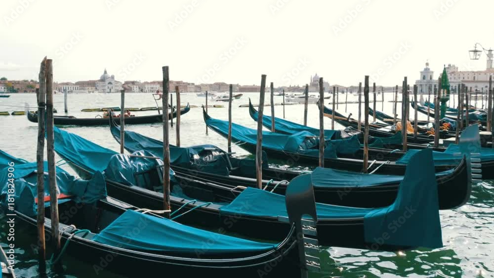 VENICE, ITALY, SEPTEMBER 7, 2017: Venetian gondola covered in blue cloth while docking on the canal in Venice Italy, Noses moored gondolas neatly standing in a row VENICE, ITALY, SEPTEMBER 7, 2017: Venetian gondola covered in blue cloth while docking on the canal in Venice Italy, Noses moored gondolas neatly standing in a row