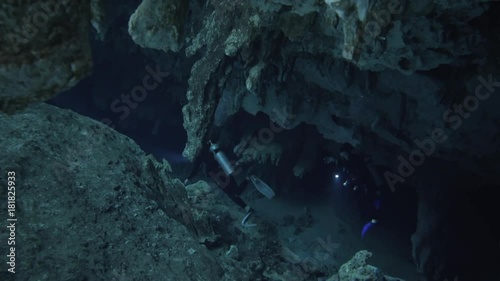 two divers underwater with flashligh swiming through stalagmite in cenote cave dos ojos