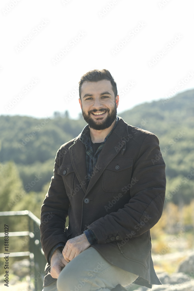 Bearded man posing in outdoors portrait looking at camera and smiling with casual clothing Bearded man posing in outdoors portrait looking at camera and smiling with casual clothing