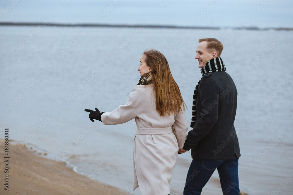 Cheerful couple walking together on the background of the coastline. Happy winter moments, enjoying time.