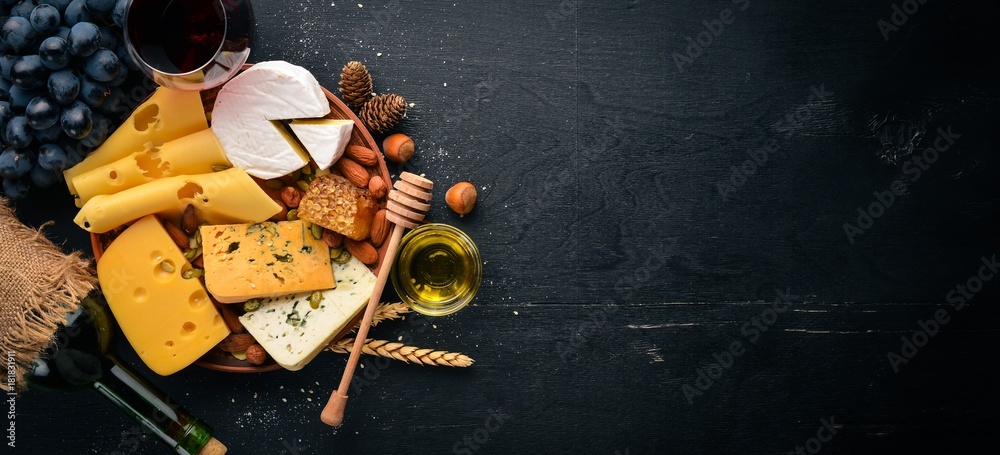 Assortment of cheeses, a bottle of wine, honey, nuts and spices, on a wooden table. Top view. Free space for text. - obrazy, fototapety, plakaty 