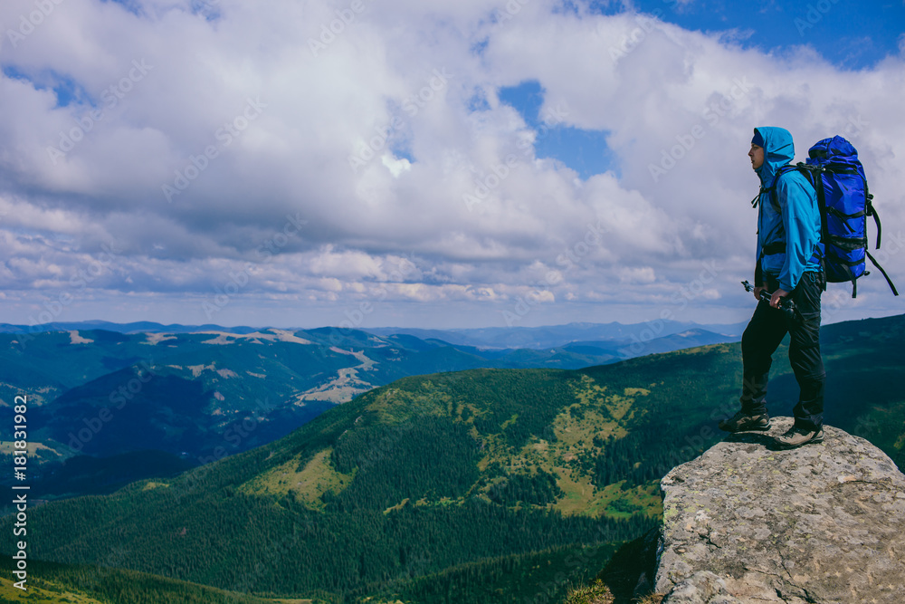 man traveler standing on the top of the mountain and looking into the mountainous landscape. Adventure and active recreation in the mountains