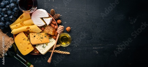 Assortment of cheeses, a bottle of wine, honey, nuts and spices, on a wooden table. Top view. Free space for text. photo