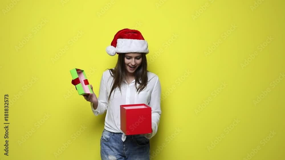 Happy christmas and new year holidays full of fun. Santa girl holding christmas gift. Smiling happy girl on yellow background. Beautiful woman, girl, female with christmas hat is posing in studio Happy christmas and new year holidays full of fun. Santa girl holding christmas gift. Smiling happy girl on yellow background. Beautiful woman, girl, female with christmas hat is posing in studio