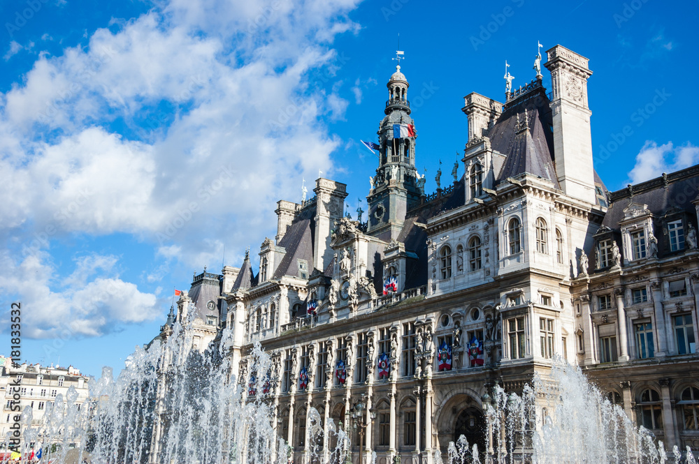 Paris City Hall (Hotel de Ville) decorated with flags and fountains in sunny day.