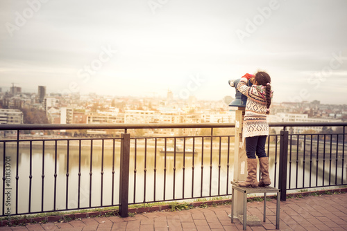 Little girl using touristic telescope and looking at city