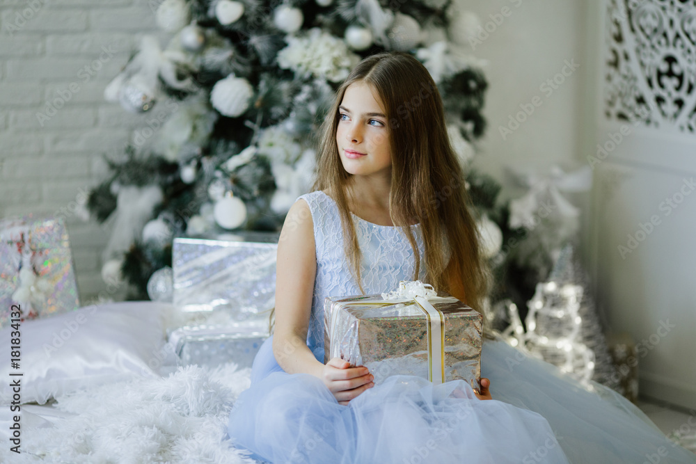 Beautiful girl is sitting near decorated christmas tree with silver gift box Beautiful girl is sitting near decorated christmas tree with silver gift box