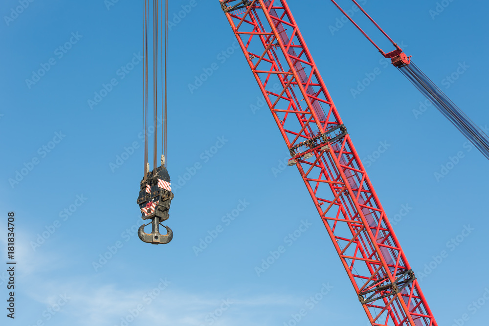 Red crane boom with steel hook against blue sky