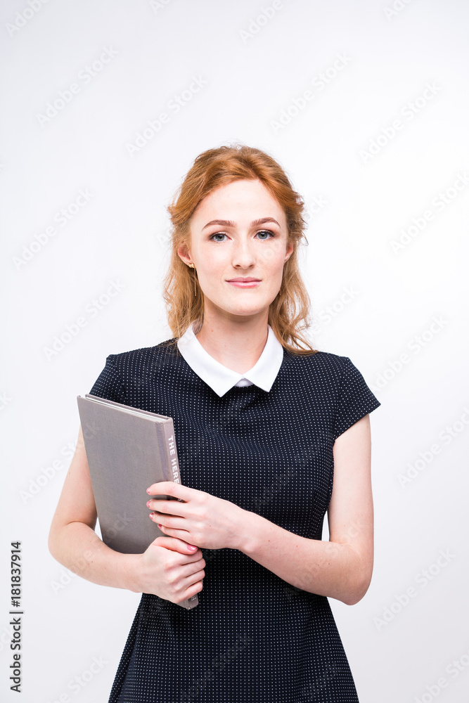 Beautiful girl with red hair and gray book in hands dressed in black dress on white isolated background Beautiful girl with red hair and gray book in hands dressed in black dress on white isolated background