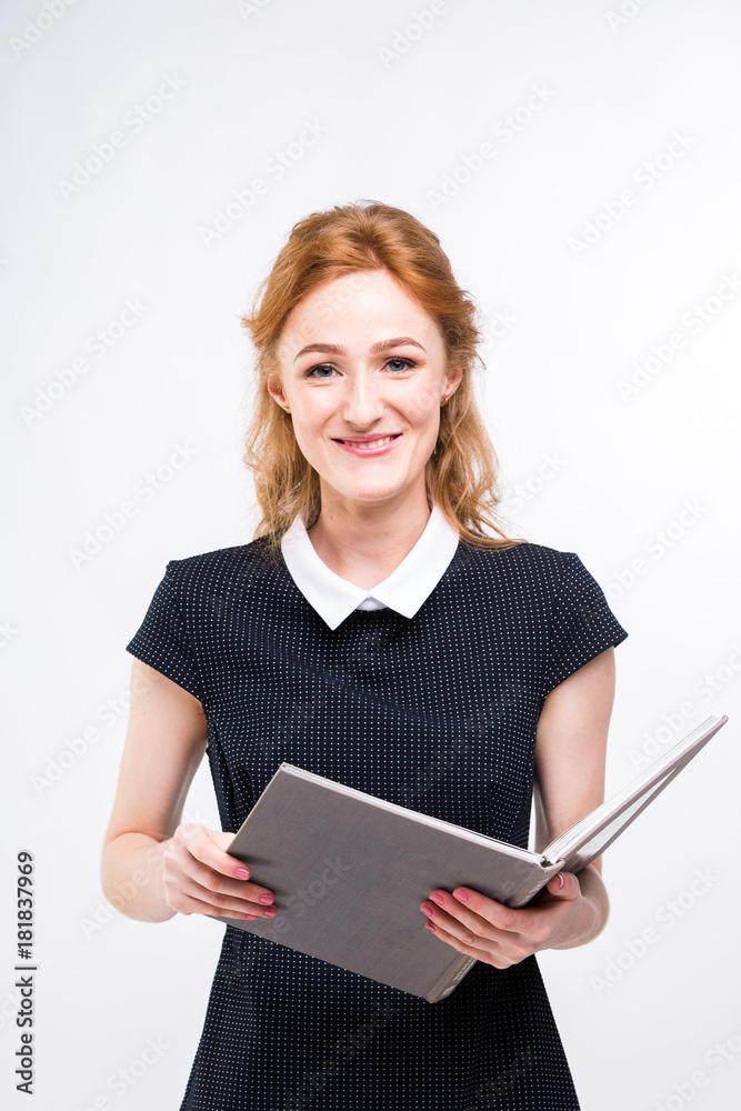 Beautiful girl with red hair and gray book in hands dressed in black dress on white isolated background Beautiful girl with red hair and gray book in hands dressed in black dress on white isolated background