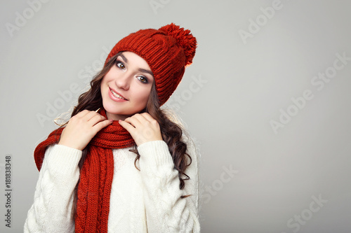 Beautiful young girl in sweater, scarf and hat on grey background
