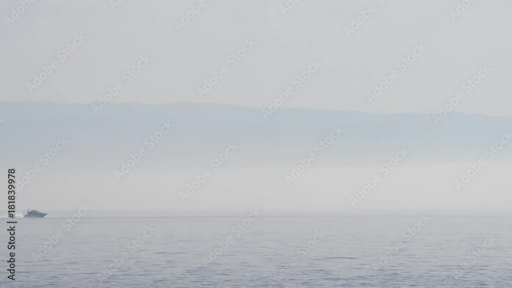 motoscafo passa all'orizzonte sul mare con foschia e la costa alle spalle motoscafo passa all'orizzonte sul mare con foschia e la costa alle spalle