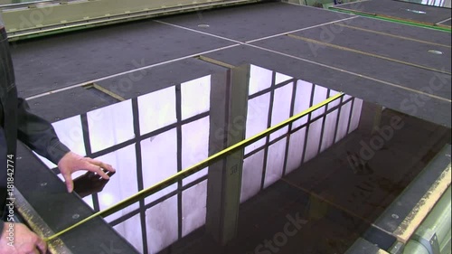 Worker measuring sheet of glass with roller on table 