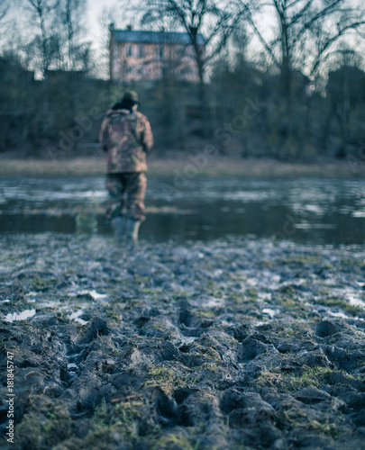 Fisherman near the river. Muddy riverbank. Focus to mud. The model is not visible and not recognizable. Vintage image effect.