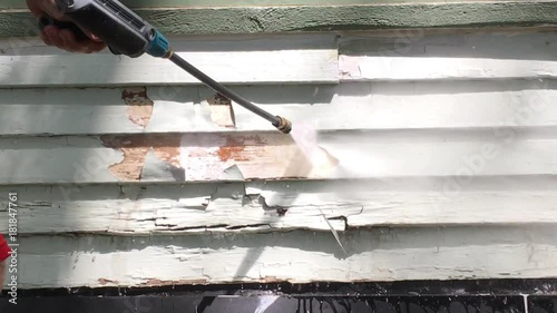 High pressure power washer blasts water onto old wood siding with paint chips flying off thereafter.  