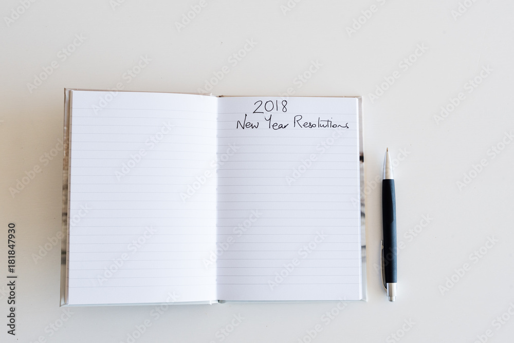 High angle view of lined journal with handwritten 2018 New Year's Resolutions heading and pen on white table (selective focus) High angle view of lined journal with handwritten 2018 New Year's Resolutions heading and pen on white table (selective focus)
