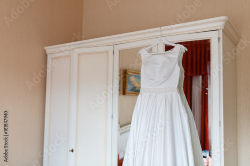 Wedding dress hanging on the wardrobe in the bedroom. The wedding collection. Classic expensive dress for a wedding or celebration in the room of an expensive hotel. Closeup