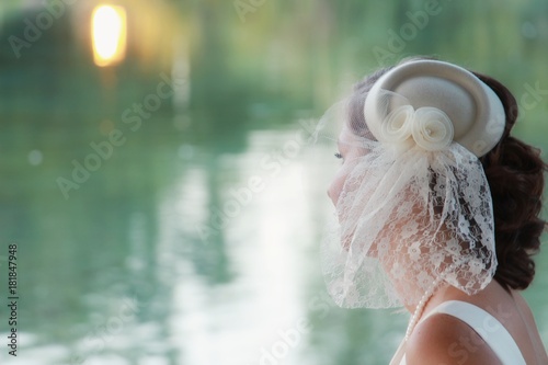 Vintage bridal wedding hairstyle of blonde bride with little hat and short veil close up water background